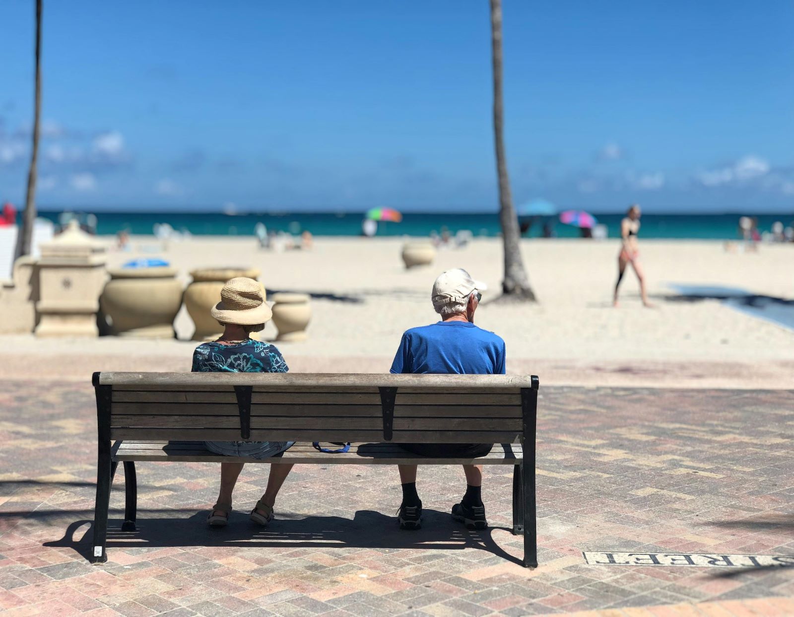 Two older adults sitting on a bench facing the ocean